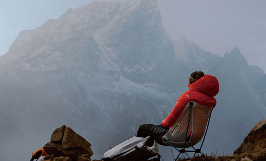 멀리 눈덮힌 산이 보이고 패등을 입은 남자가 헬리녹스체어에 앉아 먼산을 바라보고 있다